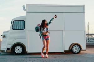 longitud completa de una joven atractiva con ropa deportiva bailando mientras se enfrenta a un camión de comida al aire libre foto