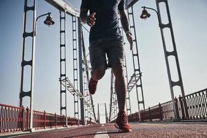 Ready to break his record. Close up of young African man in sports clothing exercising while jogging on the bridge outdoors photo