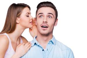 Telling secrets to him. Beautiful young women holding her mouth near ear of her boyfriend while standing against white background photo