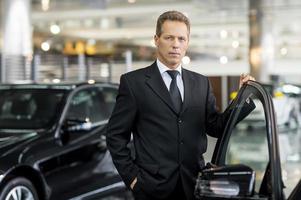 confiado en su elección. hombre de pelo gris confiado en ropa formal sosteniendo la mano en la puerta abierta del coche y mirando a la cámara foto