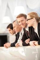 We are team. Side view of four confident business people leaning at the railing while one of them looking at camera and smiling photo