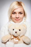 Girl with Teddy bear. Beautiful young blond hair woman holding a teddy bear and smiling while isolated on grey photo