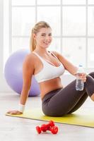 relajante después del entrenamiento. atractiva mujer madura sentada en una colchoneta de ejercicios y sosteniendo una botella con agua foto