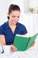 Reading her favorite book in cafe. Beautiful young woman reading book and smiling while sitting in cafe photo