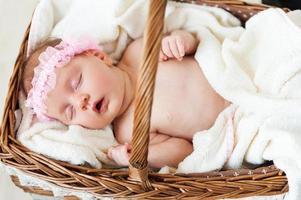 Cute baby in a basket. Top view of little baby sleeping while lying in wicker basket and covered with towel photo