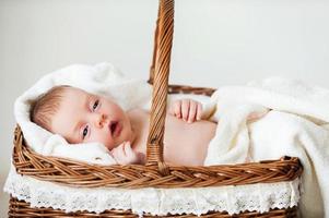 bebé en cesta de mimbre. pequeño bebé acostado en una cesta de mimbre y cubierto con una toalla foto