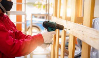 Technician use cordless drill drilling wooden box. Heavy machinery container for transport. Technician wear red coveralls, safety gloves, and protective mask during working with drilling machine. photo