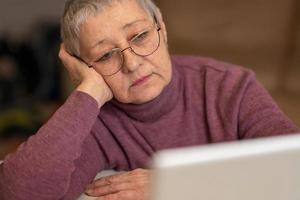 A senior woman sitting in front of a laptop communicates online through social networks. photo