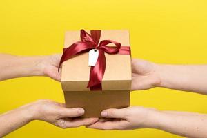 gift with a red satin ribbon is passed from hand to hand on a yellow background photo