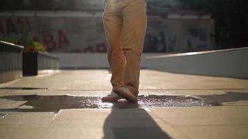 Nahaufnahme der Beine in Turnschuhen eines glücklichen Mannes, der nach dem Regen vor dem Hintergrund eines wunderschönen Sonnenuntergangslichts lustig in einer Pfütze tanzt. Zeitlupe. video