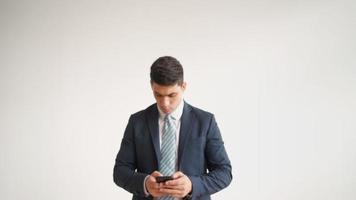 Happy male office worker in formal clothes uses a mobile phone and rejoices in victory on white background. Businessman in a jacket and tie experiences the triumph of the winner, laughs with joy. video