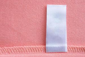 etiqueta de ropa blanca en blanco para el cuidado de la ropa sobre fondo de textura de tela rosa foto