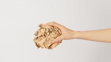 The woman's hand is holding crumpled brown paper on white background. photo