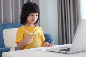 little asian girl student study online using laptop computer at home photo