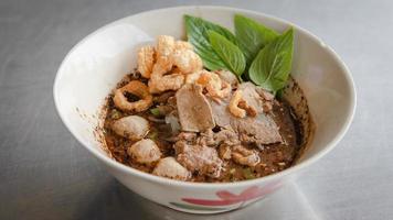 Thai Boat noodles in thicken soup added blood with Pork balls, Sliced beef and liver serve with basil and crispy fried pork skin. photo