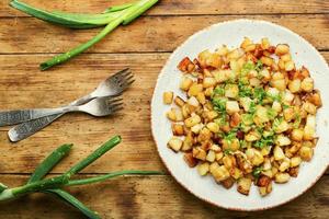 Fried potatoes with green onions,rustic wooden table photo