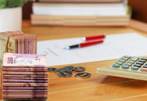 stack of banknotes and coins with calculator and blurred books on wooden table photo