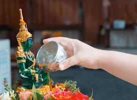 woman's hand pouring water to emerald buddha image photo