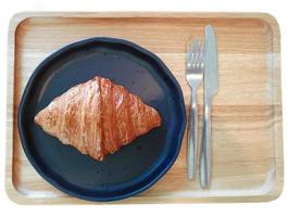 single golden croissant on dark plate with fork and spoon photo