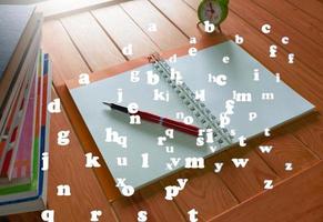 notebook and pen on wooden table with flying English alphabets photo