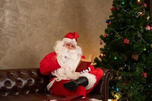 Santa claus reading red book while sitting on sofa in living room at home photo