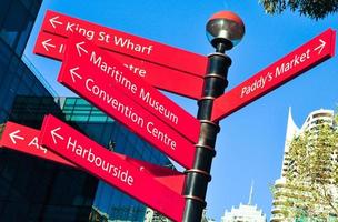Señal de flecha de direcciones rojas que apunta a lugares famosos en Darling Harbour, Sydney, Australia. foto
