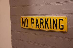 A Square Yellow vintage no parking sign on grey brick wall. photo