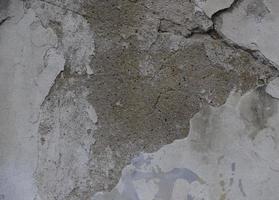 Background of peeling white paint on an old wall. Texture background of an old wall made of gray plaster. Cracks. Copy space. Old peeling plaster wall, crumbles. photo