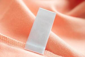 Blank white laundry care clothes label on pink fabric texture background photo