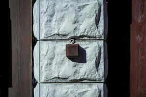 Brown square electrical switch implemented outdoors on artificial stone column betrween brown wooden planks with wire on sunny day with deep shadows photo