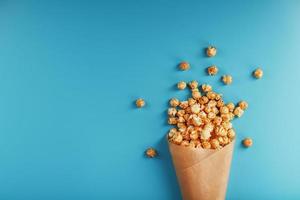 palomitas de maíz en glaseado de caramelo en un sobre de papel sobre un fondo azul. foto