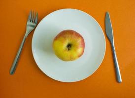 An apple in a plate, a fork and a knife photo