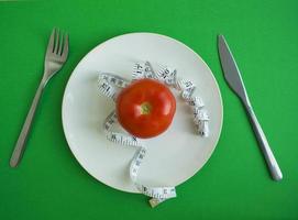 tomate y cinta centimétrica en un plato, tenedor y cuchillo foto