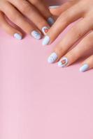 Female hands with winter snow manicure with stickers under a matte top on pink background photo