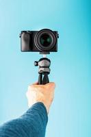 A hand holds a black SLR camera on a tripod, isolated on a blue background. photo