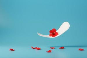 Sanitary pad in flight on a blue background with fallen petals of red flowers. Concept of the beginning of menopause. photo