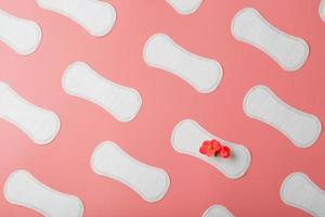 Sanitary pads on a pink background in the form of a diagonal pattern of repetitions, with a red flower on the pad. photo