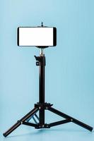 Mobile phone mounted on a tripod with a white display free for images and text, blue isolated background. photo