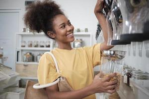 African American female customer fills cereal foods in glass jar, lever the reusable container in a refill store, and zero-waste and plastic-free grocery, environment-friendly, sustainable lifestyles. photo