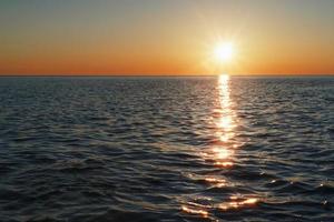 una puesta de sol soleada en el mar que se extiende hacia el horizonte con un camino y reflejos en el mar. foto