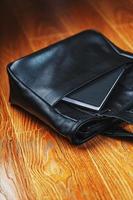 cuaderno negro que sobresale del bolsillo de un bolso de cuero negro, macro hecho a mano, materiales naturales. foto