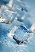 cubos de hielo de primer plano con gotas de agua derretida esparcidas sobre un fondo azul. foto