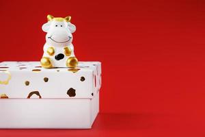 New year's toy of a cow on a box with a gift on a red background. 2021 year of the Bull, cow. photo