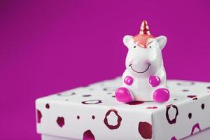 Figurine of a unicorn on the box with a gift on a pink background. photo