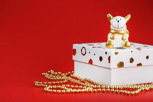 New year's 2021 toy bull with a gift on a red background. Gift box and gold beads. photo