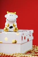 New year's 2021 toy bull with a gift on a red background. Gift box and gold beads. photo