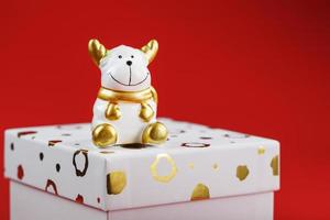 New year's 2021 toy bull with a gift on a red background. Gift box and gold beads. photo