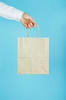 bolsa de papel con el brazo extendido, bolsa artesanal marrón para llevar aislada en fondo azul. diseño de plantilla de embalaje con espacio para copiar, publicidad. foto