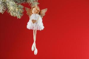juguete de ángel blanco en un árbol de navidad sobre un fondo rojo. foto
