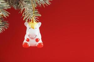 Ceramic Figure of a Unicorn on a spruce branch, on a red background. Free space for text. photo